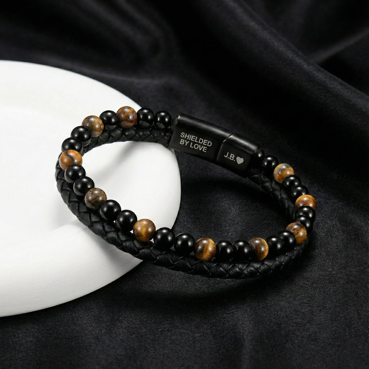 Tiger eye son bracelet with an engraved clasp displayed on contrasting black fabric and white stone